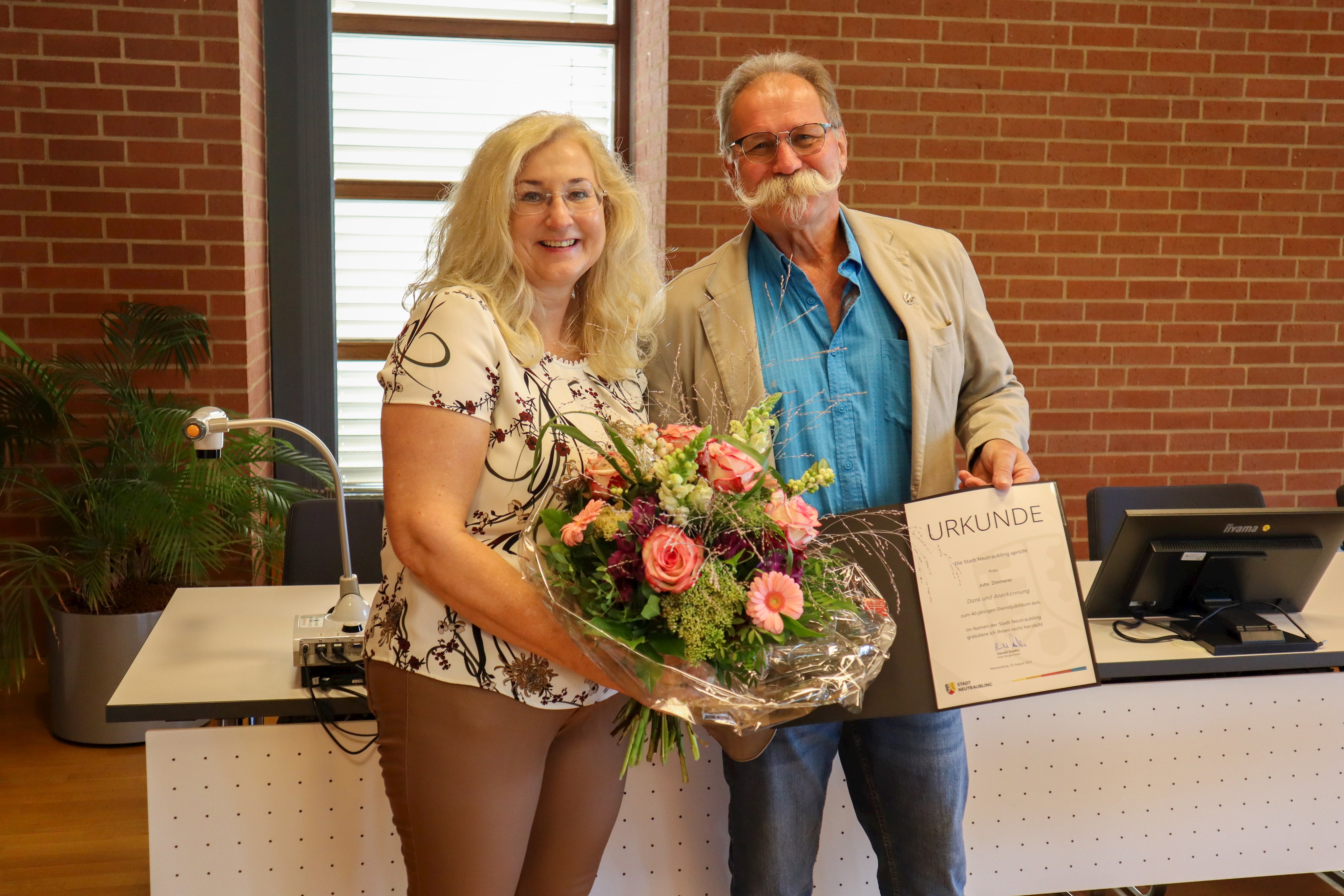 Jutta Zimmerer mit einem Blumentrauß und Ulrich Brossmann mit Urkunde